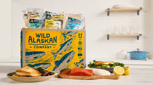 WILD ALASKAN COMPANY box with packaged Pacific Cod, Sockeye Salmon and Pacific Halibut, plus plated salmon and lemon.