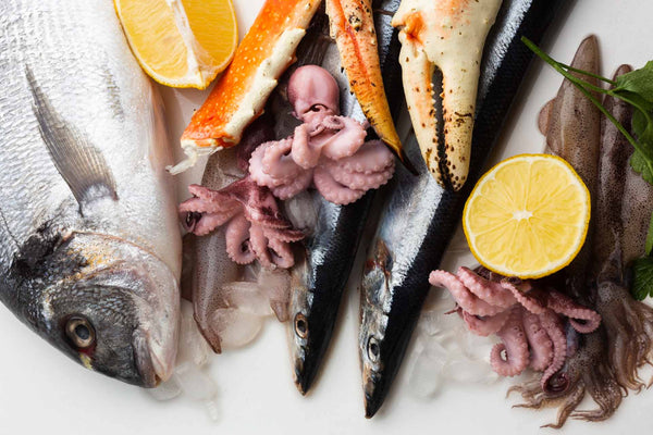 Raw seafood on ice labeled as high-cholesterol examples: whole fish, king crab claws, octopus, squid, and lemon halves