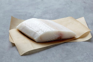 Raw black cod (sablefish) fillet on parchment paper over a gray stone surface