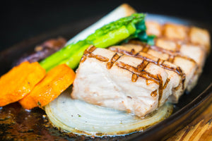 Grilled mahi‑mahi steak with asparagus, carrot slices and a grilled onion round on a hot skillet