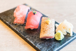 Three nigiri sushi pieces on a rectangular slate with wasabi and pickled ginger.