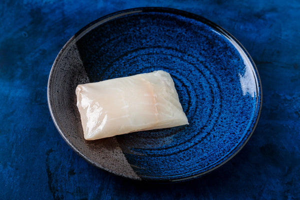 Overhead view of Alaskan halibut fillet showcasing raw, skinless white flesh on a small blue ceramic plate