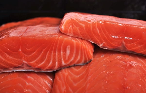Stacked raw salmon fillets with bright orange-pink flesh and white marbling