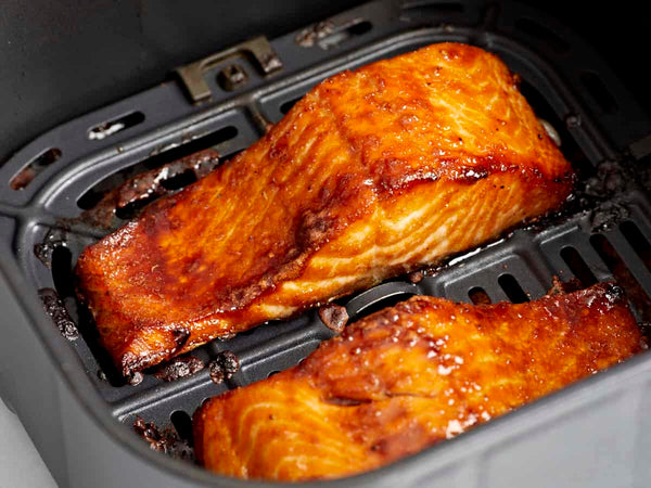 Two golden glazed Alaskan salmon fillets cooking in an air fryer basket