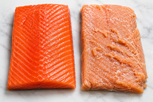 Top-down view of two salmon fillets showcasing deep red wild sockeye on the left and paler farmed salmon on white marble