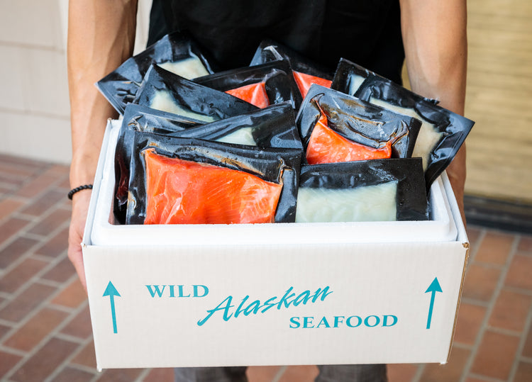 White insulated box labeled 'Wild Alaskan Seafood' filled with vacuum-sealed sockeye salmon and halibut fillets.