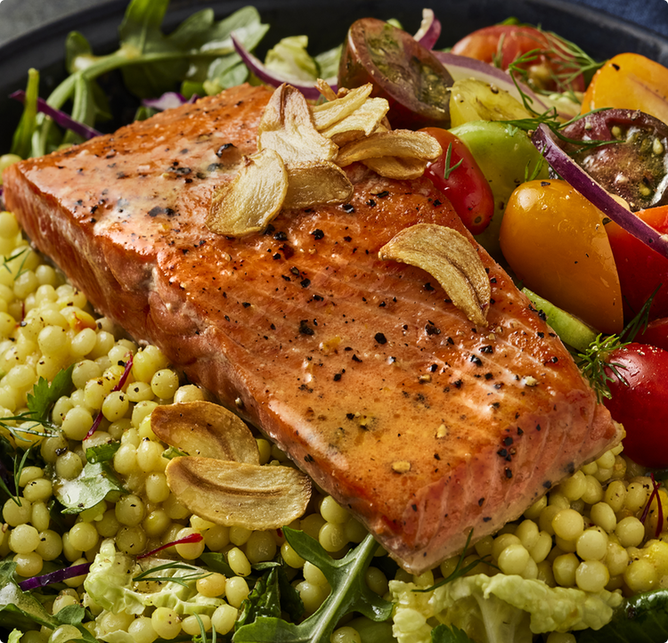 Seared wild Alaskan sockeye salmon fillet with cracked pepper and garlic chips on pearl couscous and heirloom tomato salad