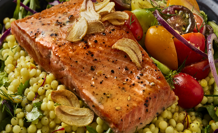 Seared Alaskan sockeye salmon fillet topped with garlic chips on pearl couscous and cherry tomato salad