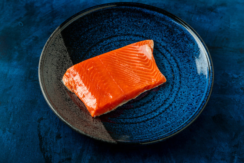 Raw salmon fillet on a blue ceramic plate against a dark background